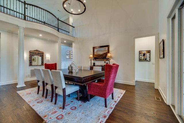 dining space featuring a towering ceiling, dark wood-type flooring, an inviting chandelier, ornamental molding, and decorative columns