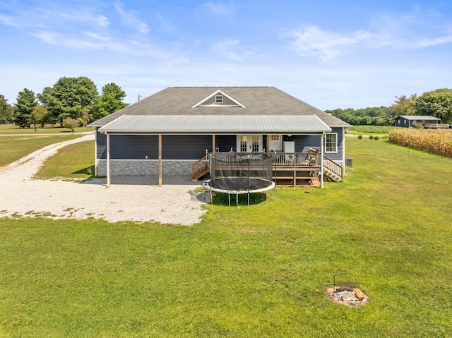 rear view of property featuring a wooden deck, a trampoline, and a yard