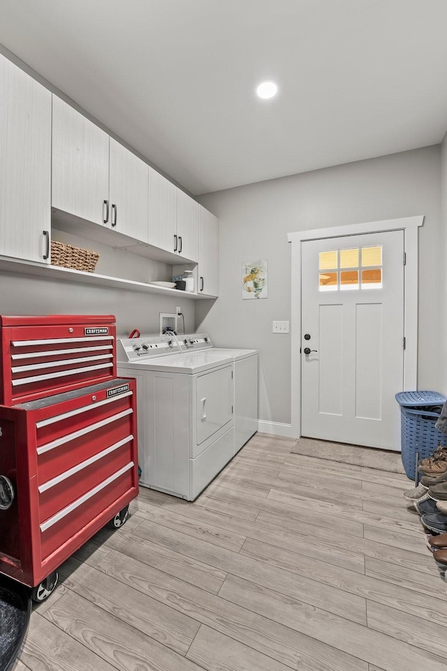 laundry area featuring washing machine and dryer, light hardwood / wood-style floors, and cabinets