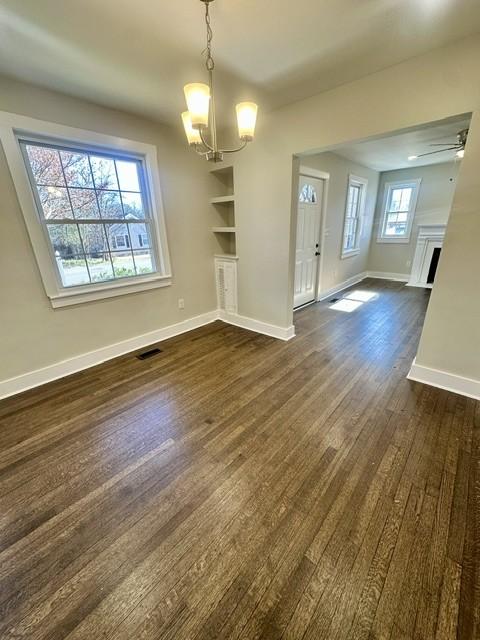 unfurnished living room featuring dark wood-type flooring, built in features, plenty of natural light, and ceiling fan with notable chandelier