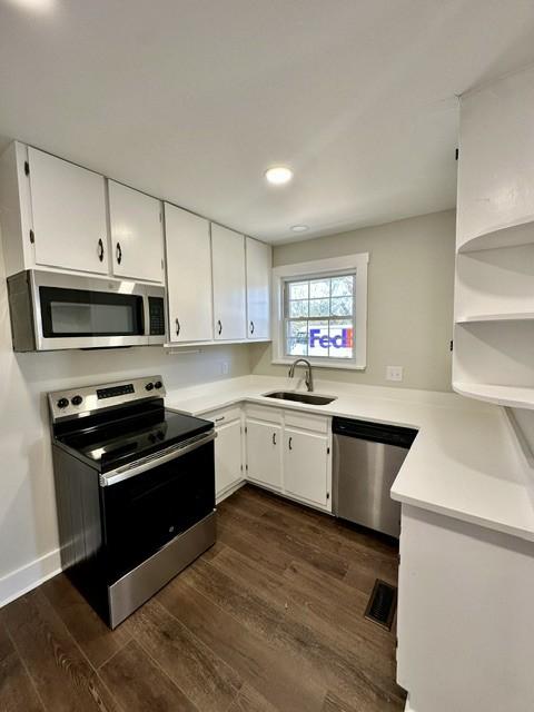 kitchen with appliances with stainless steel finishes, dark hardwood / wood-style flooring, white cabinetry, and sink