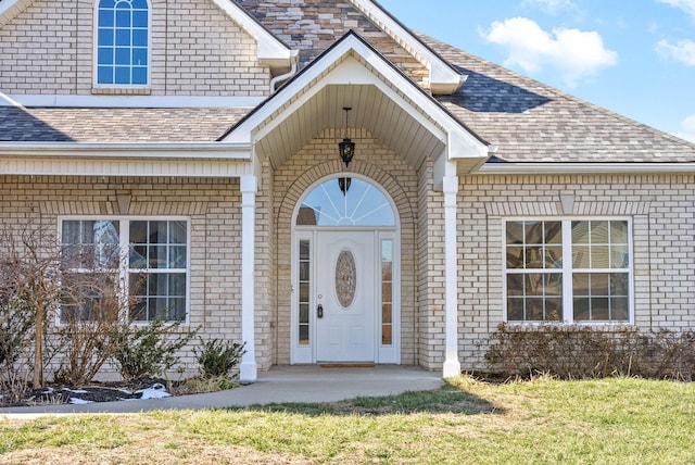 doorway to property with brick siding and roof with shingles