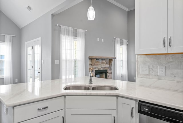 kitchen featuring dishwasher, sink, white cabinetry, a stone fireplace, and light stone counters