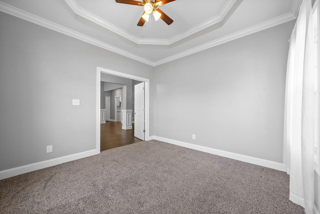 unfurnished room with ceiling fan, dark carpet, a tray ceiling, and ornamental molding