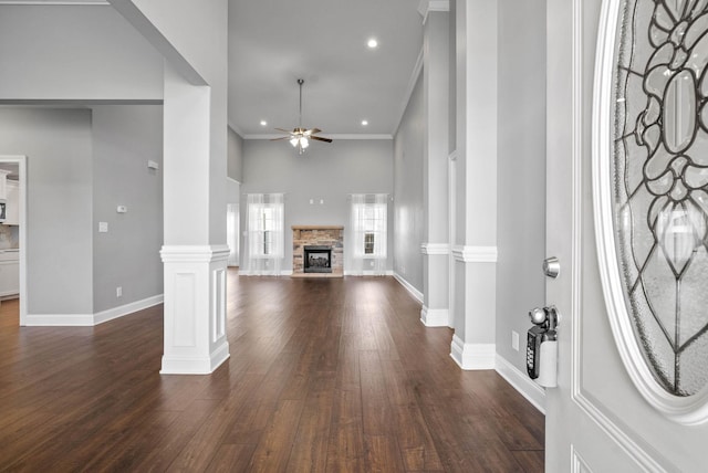 entryway featuring ornate columns, ceiling fan, dark wood-type flooring, a fireplace, and crown molding