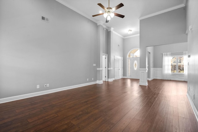 unfurnished living room with a high ceiling, ceiling fan, dark hardwood / wood-style floors, ornamental molding, and decorative columns