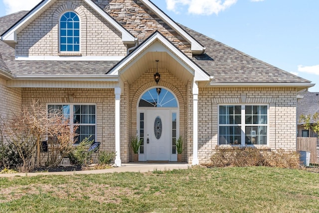 doorway to property featuring brick siding, a lawn, and a shingled roof