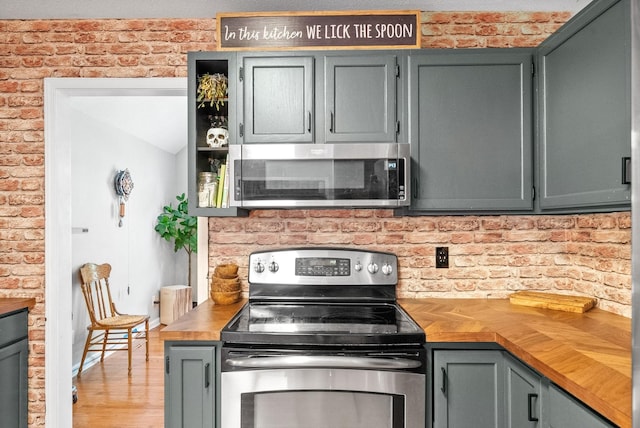 kitchen featuring wood counters, brick wall, stainless steel appliances, and light hardwood / wood-style flooring