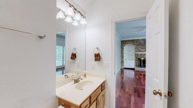 bathroom featuring a brick fireplace, hardwood / wood-style floors, vanity, and ornamental molding