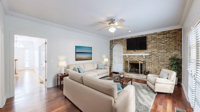 living room with a brick fireplace, wood-type flooring, ornamental molding, and ceiling fan