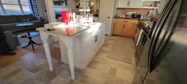 kitchen with refrigerator, a kitchen island, decorative backsplash, white cabinetry, and light stone countertops