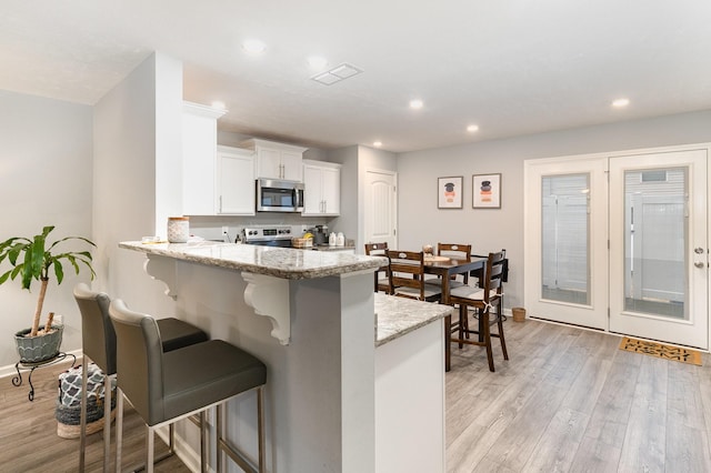 kitchen with appliances with stainless steel finishes, white cabinetry, a kitchen breakfast bar, kitchen peninsula, and light stone counters