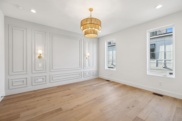 unfurnished room featuring a notable chandelier and light wood-type flooring