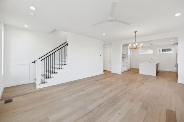 unfurnished living room featuring light hardwood / wood-style floors, sink, and ceiling fan with notable chandelier