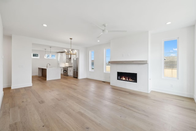 unfurnished living room featuring ceiling fan with notable chandelier, sink, and light wood-type flooring