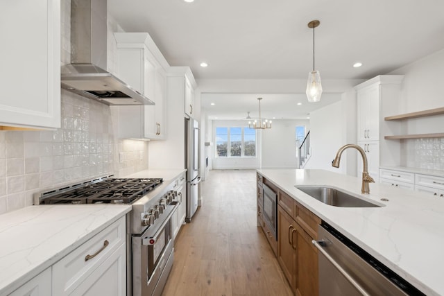 kitchen with pendant lighting, sink, high quality appliances, white cabinets, and wall chimney range hood