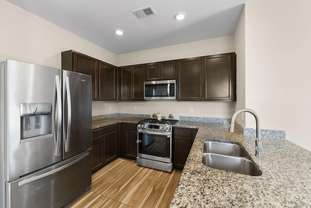 kitchen featuring light hardwood / wood-style floors, stainless steel appliances, dark brown cabinets, light stone counters, and sink