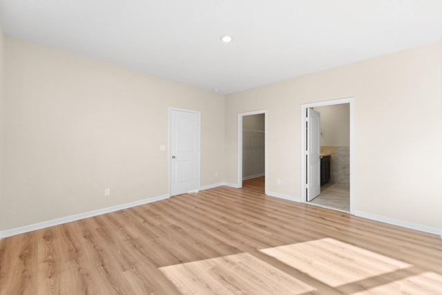 unfurnished bedroom featuring a spacious closet, a closet, connected bathroom, and light wood-type flooring