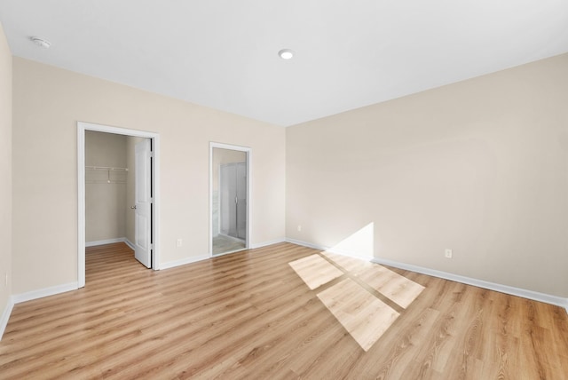 unfurnished bedroom with a spacious closet, a closet, ensuite bath, and light wood-type flooring