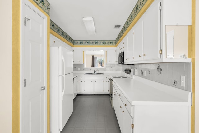 kitchen featuring stainless steel electric range oven, white refrigerator, sink, white cabinetry, and backsplash