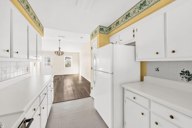 kitchen with range, white cabinetry, a chandelier, white fridge, and pendant lighting