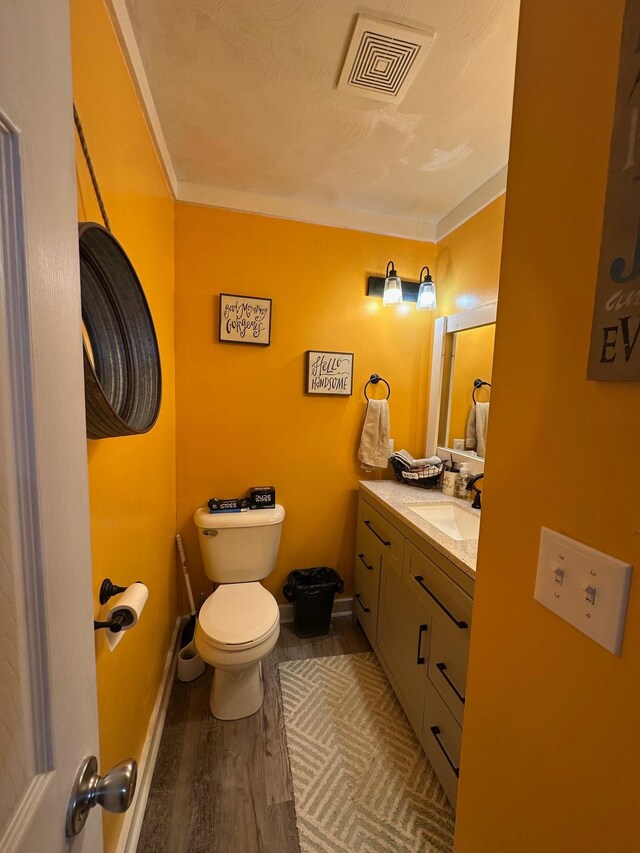 half bathroom with visible vents, toilet, vanity, wood finished floors, and baseboards