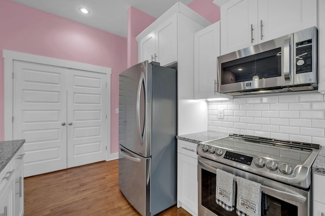 kitchen featuring decorative backsplash, light wood-type flooring, stainless steel appliances, white cabinets, and light stone counters