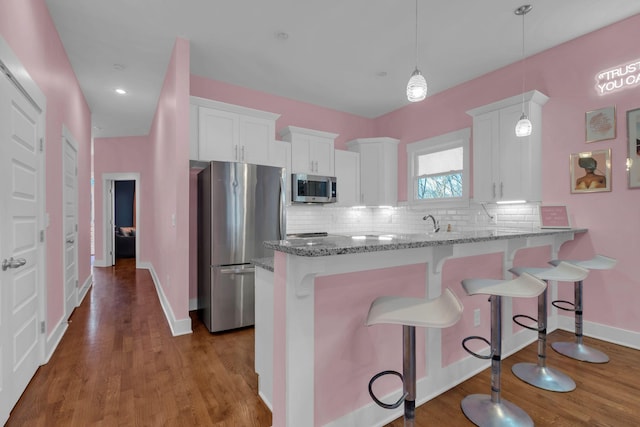 kitchen featuring backsplash, pendant lighting, kitchen peninsula, white cabinetry, and stainless steel appliances