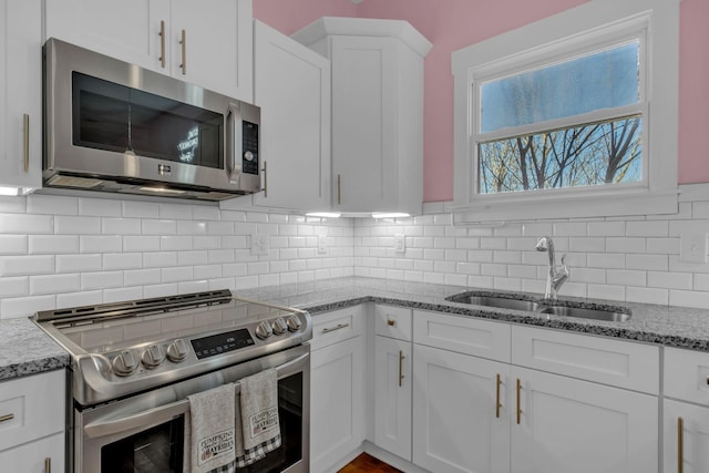 kitchen with backsplash, sink, stainless steel appliances, white cabinets, and light stone counters