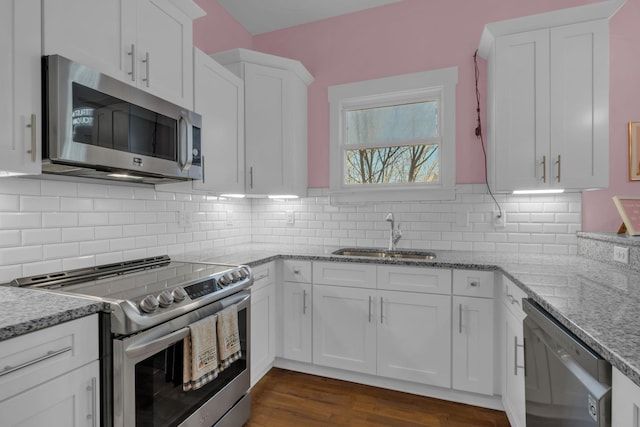 kitchen with backsplash, sink, white cabinetry, appliances with stainless steel finishes, and light stone counters