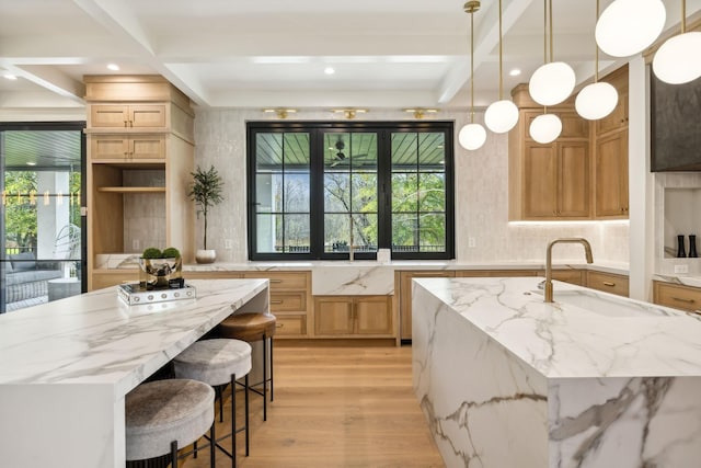 kitchen featuring sink, light hardwood / wood-style flooring, hanging light fixtures, light stone countertops, and a large island