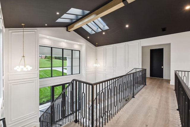 hall with a skylight, a chandelier, high vaulted ceiling, light hardwood / wood-style flooring, and beam ceiling