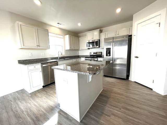 kitchen with dark stone countertops, a kitchen island, dark wood-type flooring, stainless steel appliances, and white cabinets