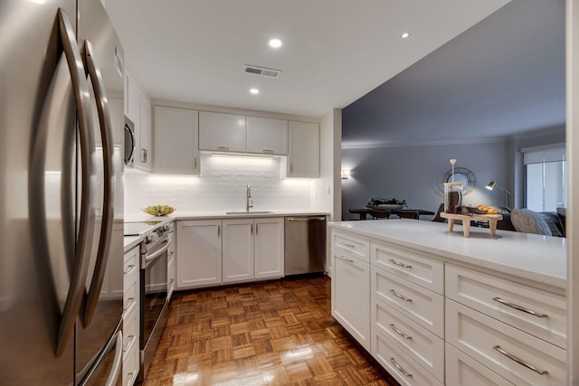 kitchen with white cabinets, dark parquet flooring, stainless steel appliances, decorative backsplash, and sink