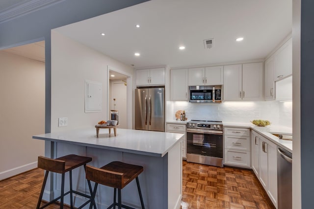 kitchen with appliances with stainless steel finishes, white cabinetry, backsplash, dark parquet floors, and a breakfast bar