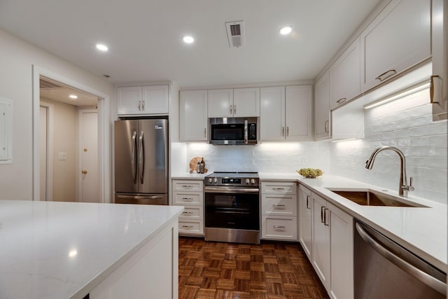 kitchen featuring dark parquet floors, appliances with stainless steel finishes, sink, and white cabinetry