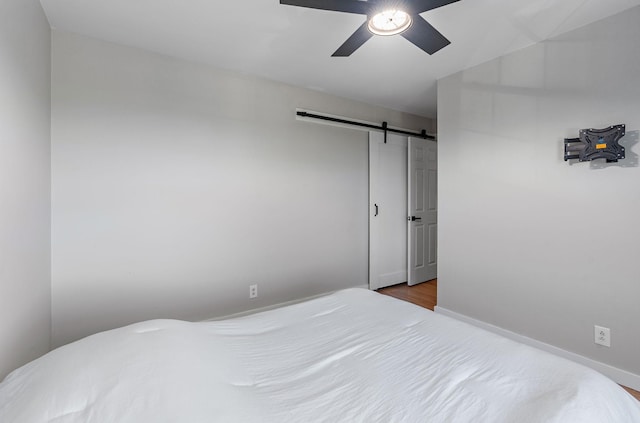 bedroom featuring ceiling fan, a barn door, and hardwood / wood-style flooring