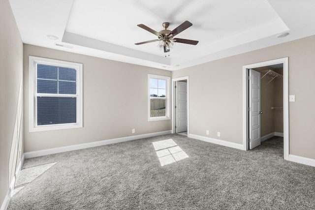 unfurnished bedroom featuring ceiling fan, a walk in closet, and a tray ceiling