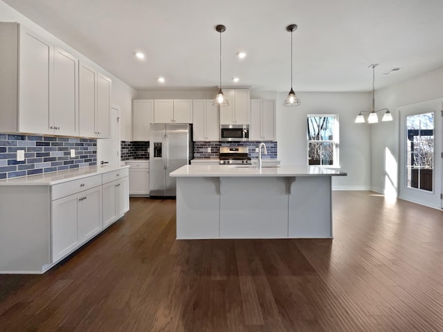 kitchen with appliances with stainless steel finishes, dark hardwood / wood-style floors, a kitchen island with sink, decorative light fixtures, and white cabinets