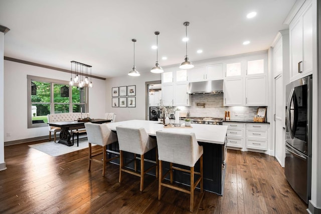 kitchen featuring white cabinetry, stainless steel fridge, an island with sink, decorative light fixtures, and ornamental molding