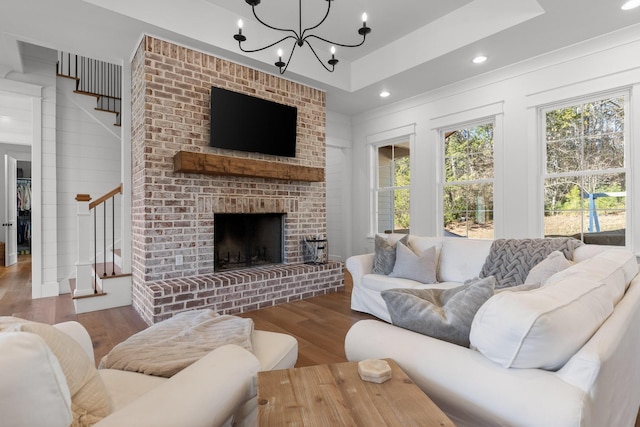 living room featuring a brick fireplace, hardwood / wood-style floors, a raised ceiling, and an inviting chandelier