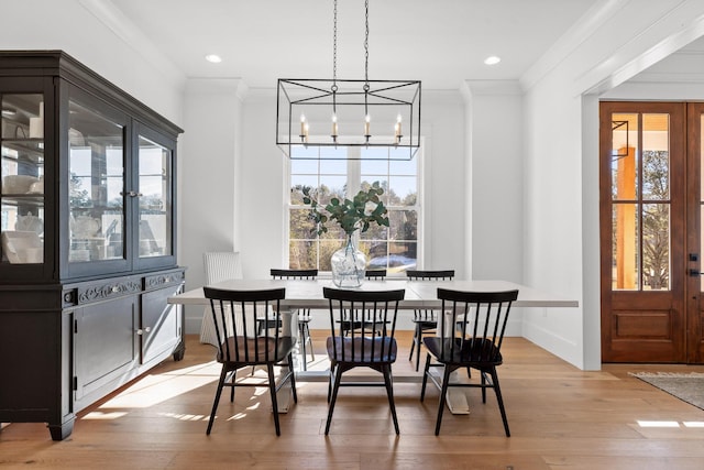 dining area with light wood-type flooring, ornamental molding, and a notable chandelier