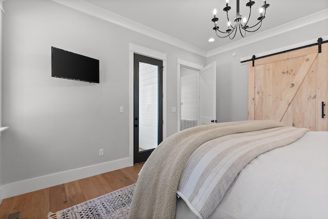 bedroom featuring a chandelier, hardwood / wood-style floors, ornamental molding, and a barn door