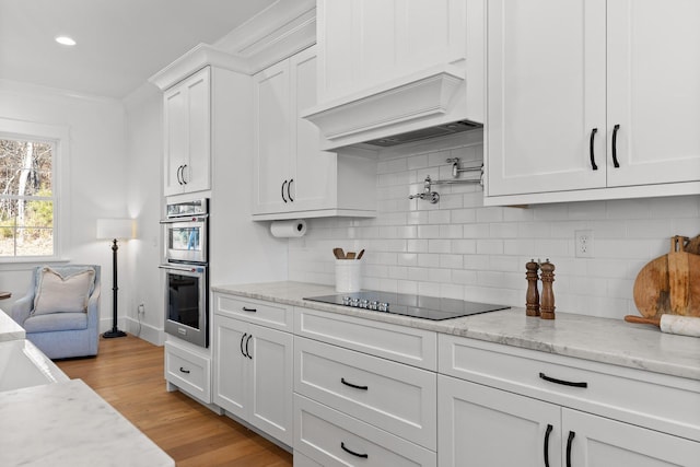 kitchen with light stone countertops, white cabinets, custom exhaust hood, black electric stovetop, and tasteful backsplash