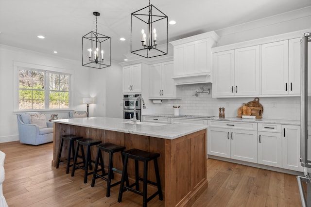 kitchen featuring light stone counters, pendant lighting, white cabinets, and a kitchen island with sink