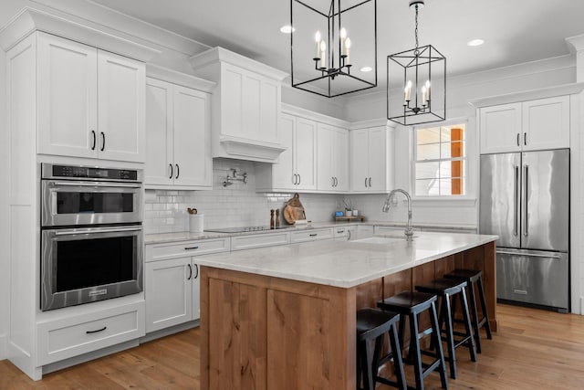 kitchen with appliances with stainless steel finishes, sink, white cabinetry, and an island with sink