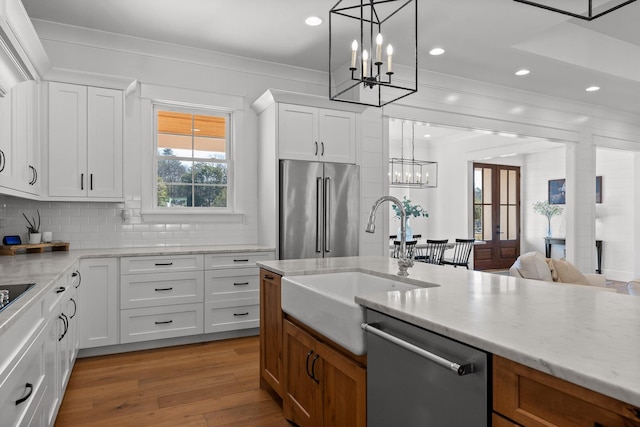 kitchen with decorative light fixtures, sink, white cabinetry, stainless steel appliances, and light stone counters