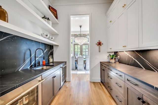 kitchen featuring backsplash, light hardwood / wood-style floors, sink, white cabinetry, and a chandelier