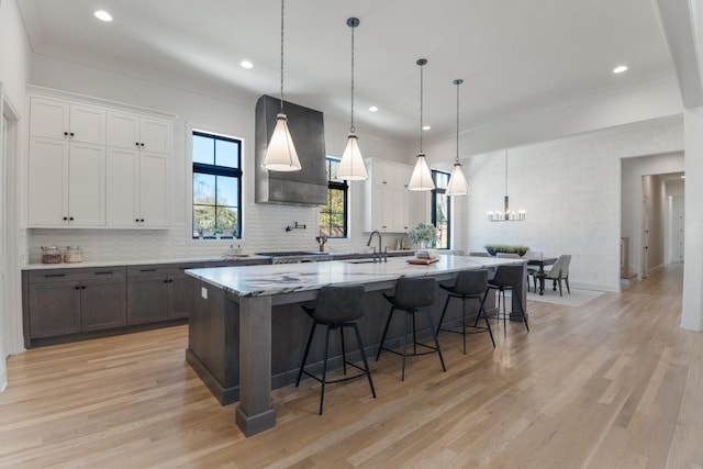 kitchen featuring decorative light fixtures, exhaust hood, a spacious island, white cabinetry, and light wood-type flooring