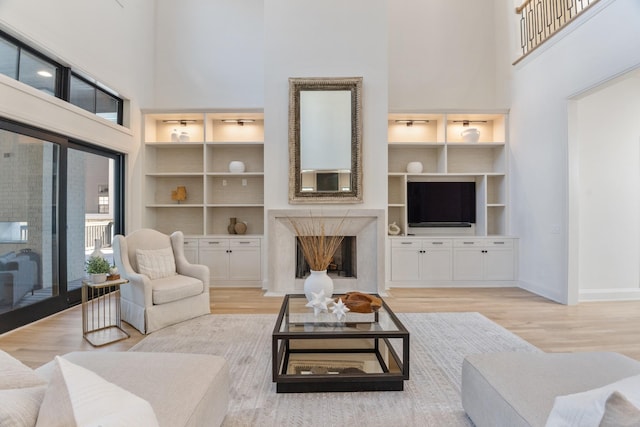 living room with a premium fireplace, light hardwood / wood-style floors, a towering ceiling, and built in shelves